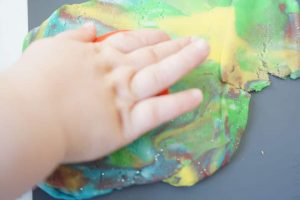 Kinderhand auf einem Haufen Knete aus verschiedenen gemischten Farben - DIY mit Kindern: selbstgemachte Knete ohne Alaun