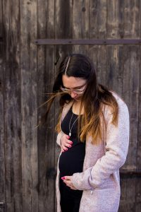 Mama in der 18. Woche schwanger, hält beide Hände an den Bauch