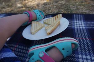 Mittagssnack für breifrei und BLW Kleinkinder im Urlaub - Sandwich auf einem Teller, danaeben Kinderfüße in mint und pink farbenen Sandalen von Crocs