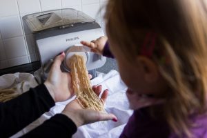 Mädchen bereitet Nudeln selbst zu und hält die aus der Nudelmaschine kommende Pasta fest