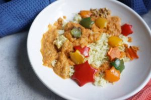 weißer Teller mit Reis und oraangefarbener paprika Zucchini Soße und Sternen aus Gemüse ausgestochen - Gemüsesoße für Kinder