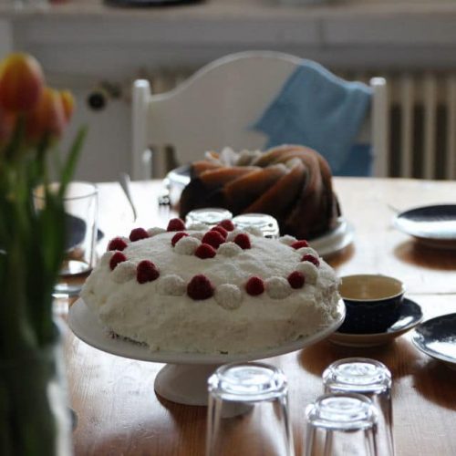 Raffaellotorte mit Himbeeren auf gedeckter Kaffeetafel für den Muttertag mit Tulpen und Mamorkuchen