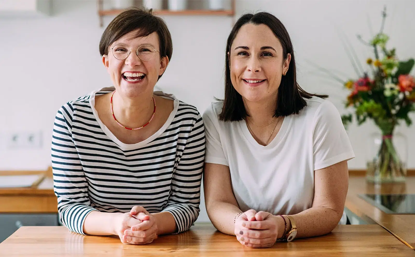 Lena und Annina von breifreibaby lehnen sich nebeneinander auf eine Kücheninsel und lächeln freundlich in die Kamera